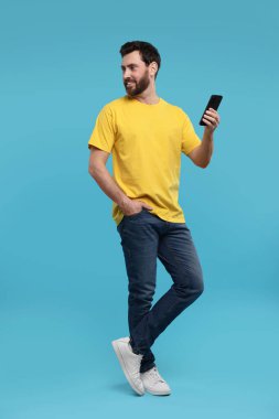 Açık mavi arka planda akıllı telefonu olan yakışıklı bir adam.