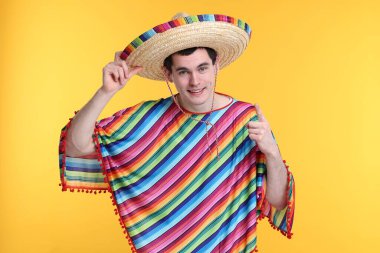 Sarı arka planda Meksika şapkalı ve pançolu genç adam.