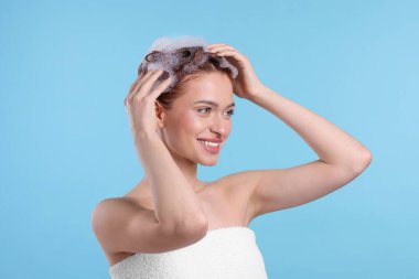Saçı açık mavi arka planda şampuanla yıkanan mutlu genç bir kadın.