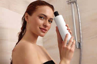 Duşta şampuan şişesiyle mutlu genç bir kadın.