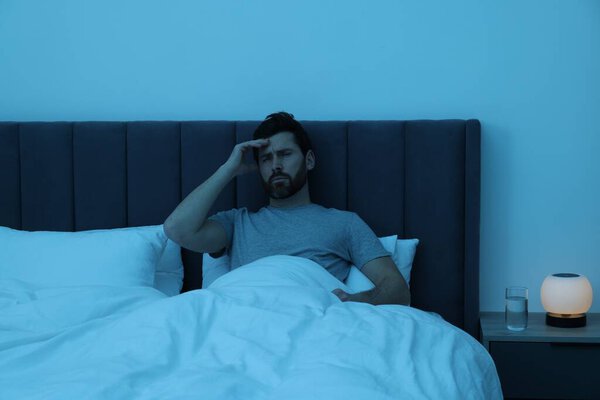 Мужчина, страдающий от головной боли в постели ночью