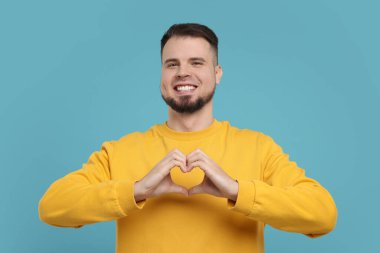 Elleri açık mavi arkaplanda kalp hareketi gösteren bir adam.