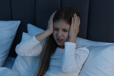 Küçük kız gece yatağında baş ağrısı çekiyor.