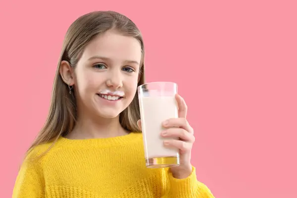 ミルクの口ひげを持つ幸せな少女は ピンクの背景に美味しい乳製品の飲み物のグラスを保持しています テキスト用スペース — ストック写真