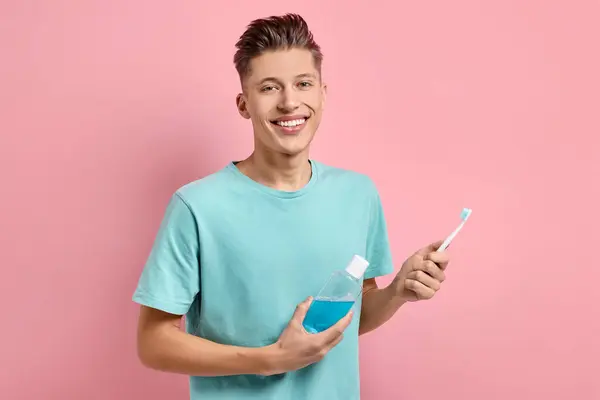 ピンクの背景にマウスウォッシュと歯ブラシを持つ若い男 — ストック写真