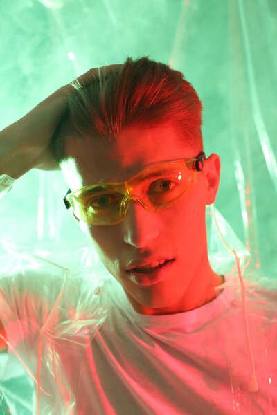 Stylish young man wearing clear coat and glasses in neon lights