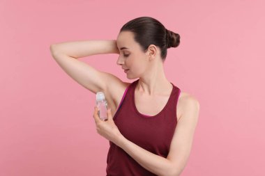 Güzel bir kadın pembe arka plana deodorant sürüyor.