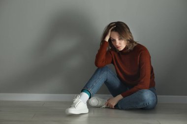 Gri duvarın yanında yerde oturan üzgün genç kadın, mesaj için yer var.