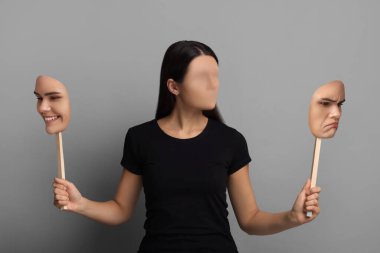 Yüz maskelerini tutan yüzü olmayan kadın gri arka planda farklı duygular gösteriyor. Kişilik krizi.