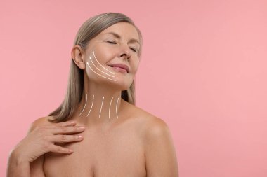 Pembe arka planda kozmetik tedaviden sonra mükemmel bir cilde sahip bir kadın. Okları boynuna ve yüzüne doğru kaldırıyor.