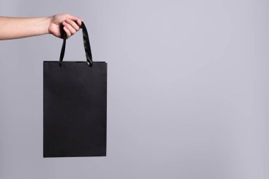 Gri arka planda kağıt alışveriş torbası tutan kadın, yakın plan. Metin için boşluk