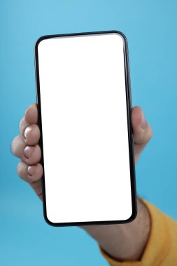 Açık mavi arkaplanda boş ekranlı akıllı telefonu tutan adam, yakın plan