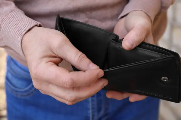 Poor man holding empty wallet outdoors, closeup