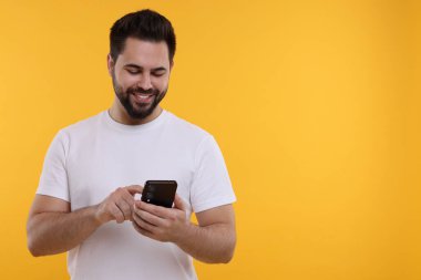 Mutlu genç adam sarı arka planda akıllı telefon kullanıyor, mesaj için boşluk