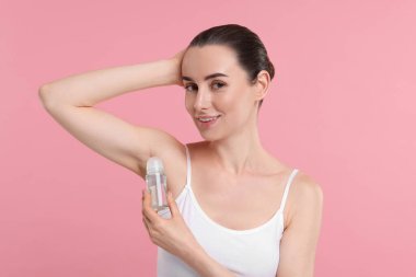 Güzel bir kadın pembe arka plana deodorant sürüyor.