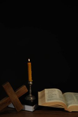 Kilise mumu, İncil ve haç, siyah arka plana karşı ahşap masada.