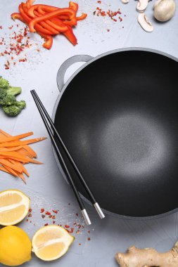 Wok, yemek çubukları ve farklı ürünler gri masada, düz yerde.