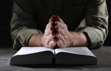 Din. Hıristiyan adam masada İncil için dua ediyor, yakın plan.
