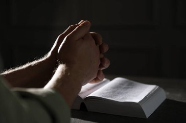 Din. Hıristiyan adam masada İncil için dua ediyor, yakın plan. Metin için boşluk
