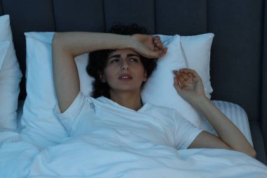 Geceleri yatakta baş ağrısı çeken genç bir kadın.