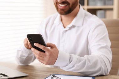 Ofiste akıllı telefon kullanan gülümseyen adam, yakın plan.