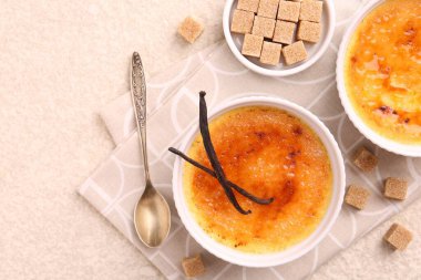 Lezzetli creme brulee kaseler, vanilya kabukları, şeker küpleri ve kaşık ışık desenli masa, üst görünüm