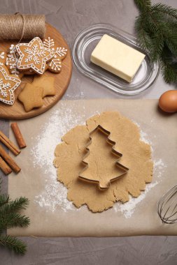 Noel kurabiyesi yapıyorum. Gri masa üzerinde malzemeler ve ham hamur içeren düz bir kompozisyon.