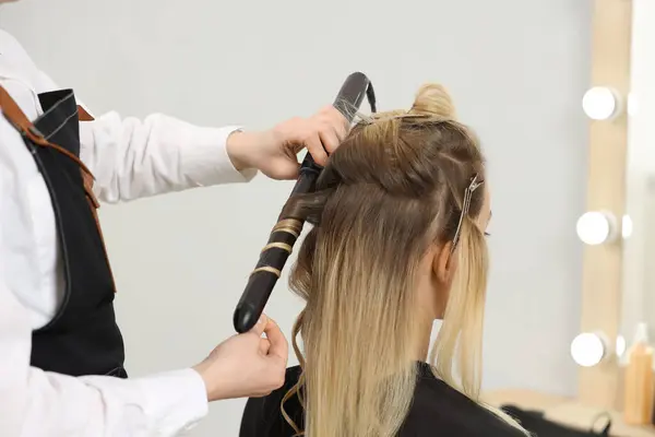 Hair styling. Hairdresser curling woman\'s hair in salon, closeup