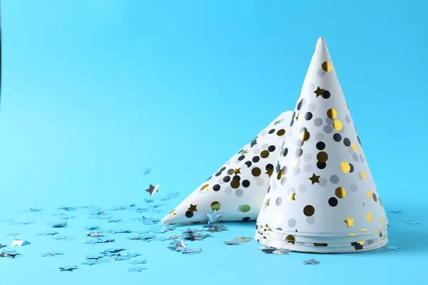 Party hats and confetti on light blue background, space for text