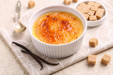 Lezzetli creme brulee kasede, vanilya kabukları ve şeker küpleri açık dokulu masada, yakın plan