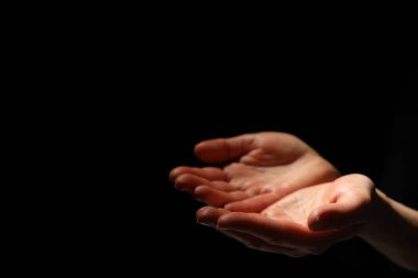 Din. Avuç içi açık bir kadın siyah arka planda dua ediyor, yakın plan. Metin için boşluk