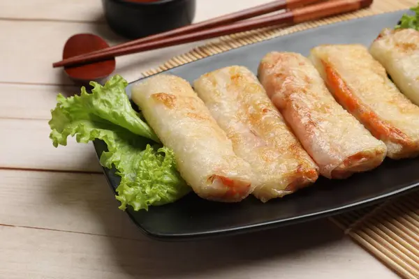 Delicious fried spring rolls and chopsticks on light wooden table, closeup