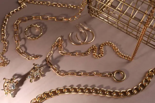 Metal chains and other different accessories on light brown background, above view. Luxury jewelry