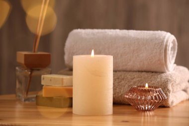 Spa kompozisyonu. Yanan mumlar, havlular, sabun ve kamış oda spreyi ahşap masada, yakın plan.