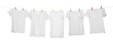 Çamaşır ipinde kuruyan birçok tişört beyaza izole edilmiş.