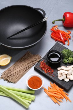 Wok, yemek çubukları ve gri masadaki farklı ürünler.