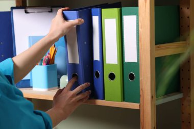 İçerideki raflardan klasör ofis klasörünü alan kadın.