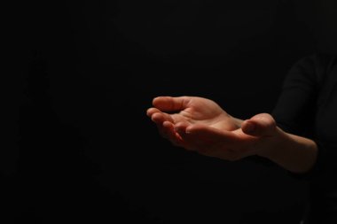 Din. Avuç içi açık bir kadın siyah arka planda dua ediyor, yakın plan. Metin için boşluk