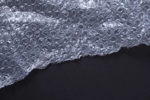 Transparent bubble wrap on black background, top view. Space for text
