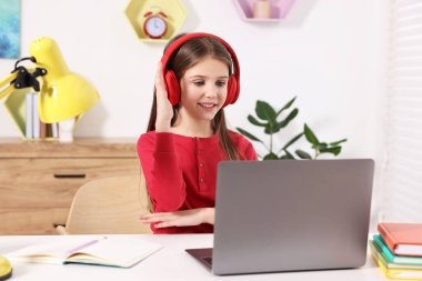 E-öğrenme. İçerideki masada çevrimiçi ders sırasında cevap vermek için elini kaldıran tatlı kız.