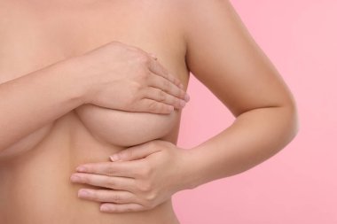 Mammoloji. Çıplak kadın pembe arka planda göğüs muayenesi yapıyor, yakın plan.