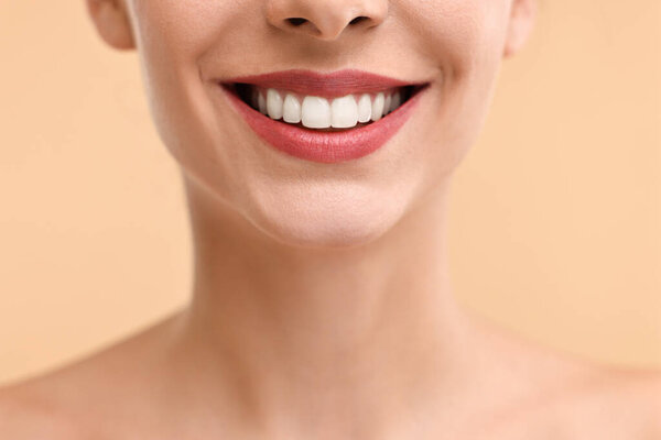 Woman with beautiful lips smiling on beige background, closeup