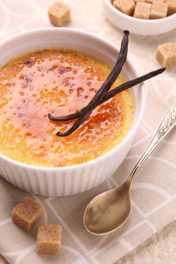 Lezzetli creme brulee kasede, vanilya kabukları, şeker küpleri ve kaşık masada, yakın çekim