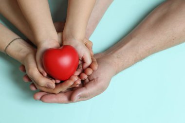 Açık mavi arkaplanda kırmızı dekoratif kalp taşıyan aileler ve çocuklar, üst görünüm