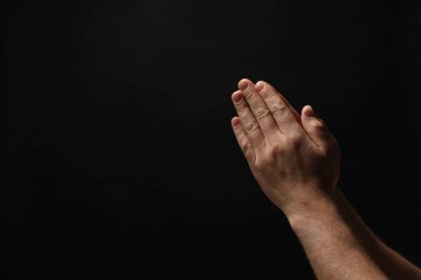 Din. Hıristiyan adam siyah arka planda dua ediyor, yakın plan. Metin için boşluk