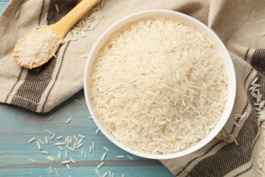 Tabakta çiğ basmati pilavı ve açık mavi ahşap masada kaşık, üst manzara.