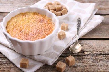 Lezzetli creme brulee kasede, şeker küpleri ve kaşık ahşap masada, yakın plan