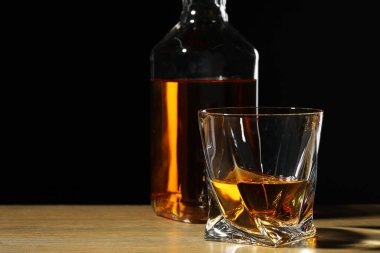 Bardakta viski ve siyah arka plana karşı ahşap masada şişe. Metin için boşluk