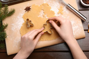 Ahşap masada kesicilerle Noel kurabiyesi yapan kadın.