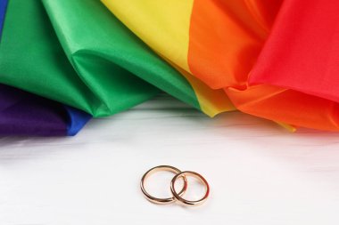 Gökkuşağı LGBT bayrağı ve alyanslar beyaz ahşap masada, yakın plan